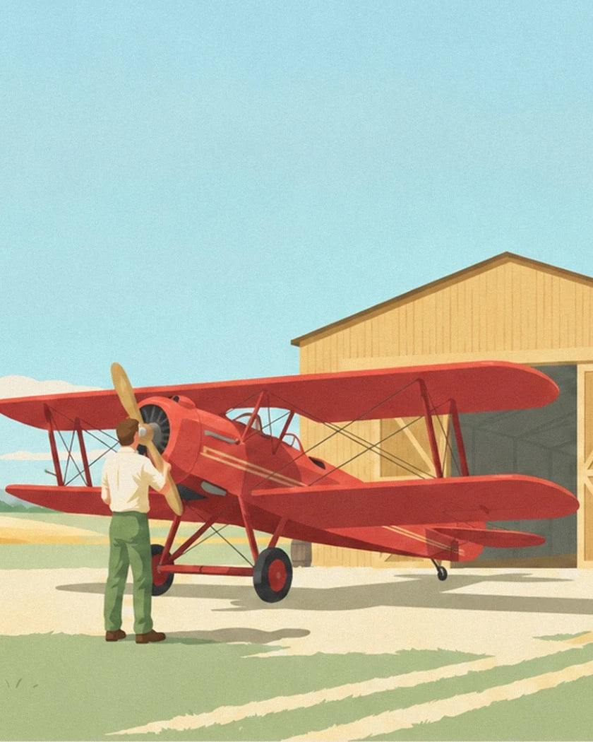 The pilot in a white shirt facing the red biplane, in front of the wooden hangar